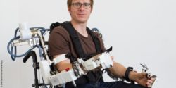 Image: Man in a wheelchair with robotic-supported system on the upper body; Copyright: DFKI GmbH/Annemarie Popp