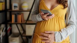 Image: Pregnant woman in a yellow dress is looking at her phone; Copyright: DragonImages