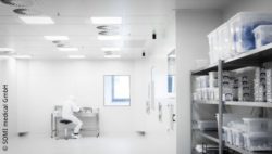 Image: Clean room of SOMI medical, in the rear area is working an employee, in the front area at the right is a filled storage rack; Copyright: SOMI medical GmbH