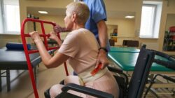 A nurse helps a woman in rehab to get up from a wheelchair – exoskeletons in the hospital