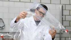 Image: In the foreground, there is a transparent tiny mattress designed for newborns. The mattress is held by a man in a smock, wearing glasses; Copyright: Empa 