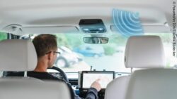 Image: Photo of a car interior. A man sits behind the wheel and operates a screen; Copyright: Fraunhofer IDMT/Anika Bödecker 