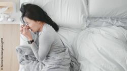 Image: A sick woman in lying in bed, blowing her nose and wearing a smartwatch at her wrist; Copyright: PantherMedia/ryanking999
