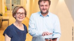 Image: Professor Dr. Anna-Maria Dittrich and Dr. Matthias Gietzelt (with tablet) stands in a building passage and smiles for the camera; Copyright: Karin Kaiser / MHH