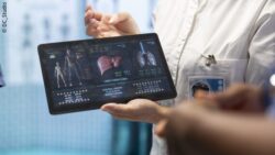 Female physician holding a tablet displaying various graphics and data about a person – medicine of the future; Copyright: DC_Studio